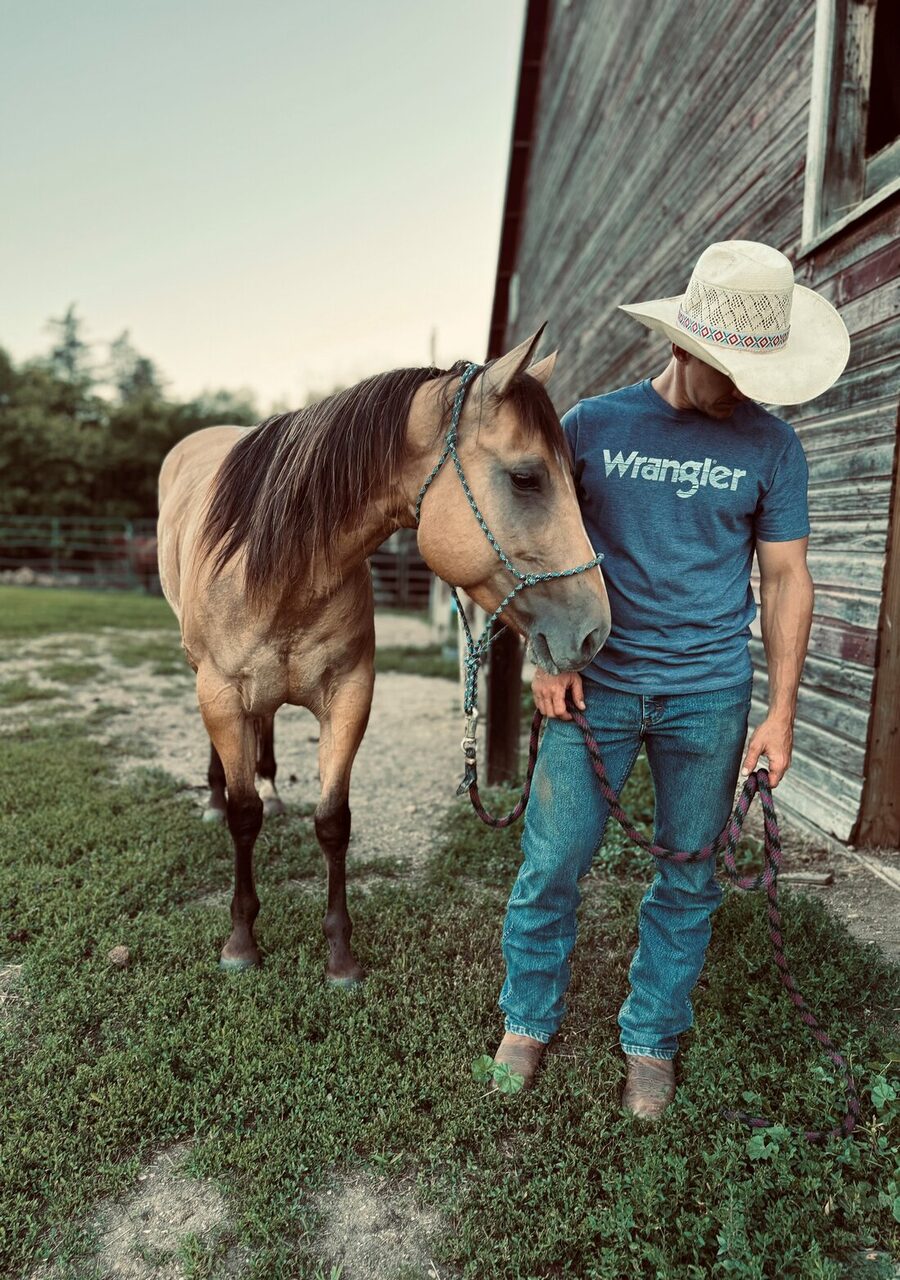 Jon Anderson leading his horse beside a weathered barn
