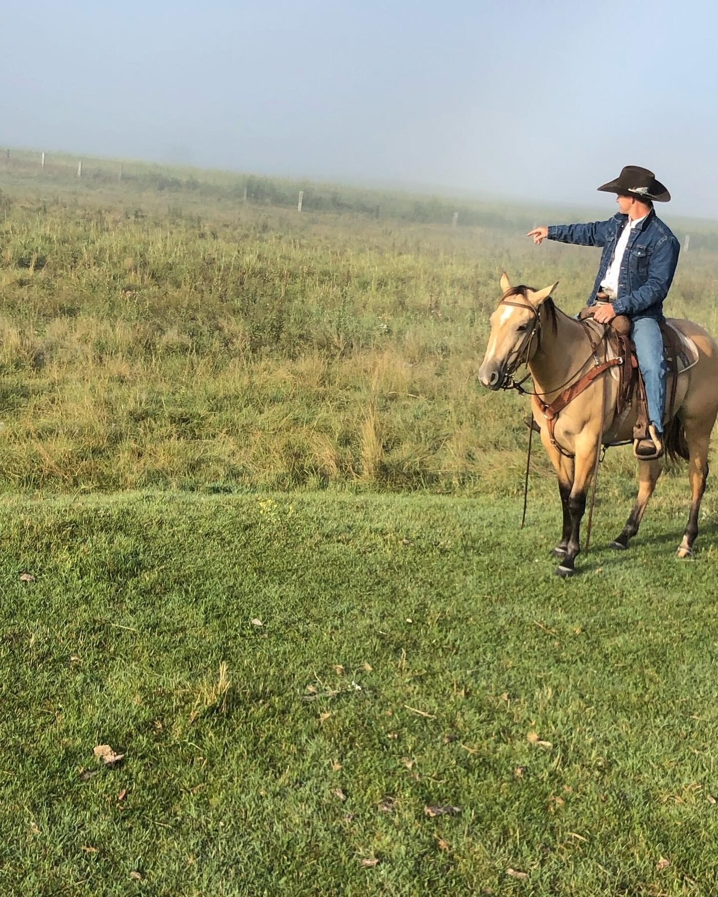 Jon Anderson pointing across a foggy pasture from horseback